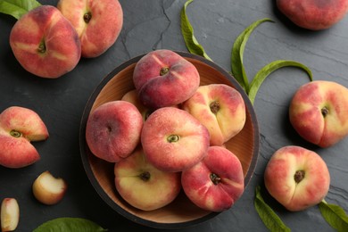Photo of Fresh ripe donut peaches with leaves on dark table, flat lay