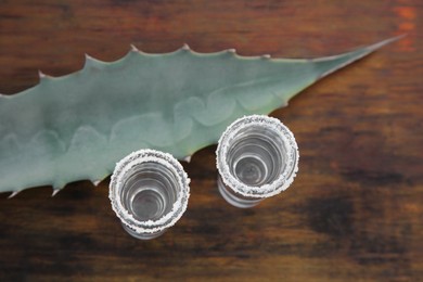 Photo of Mexican tequila shots with salt and green leaf on wooden table, top view. Drink made of agava