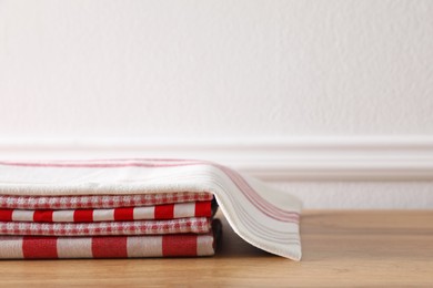 Photo of Stack of kitchen towels on wooden table near white wall. Space for text