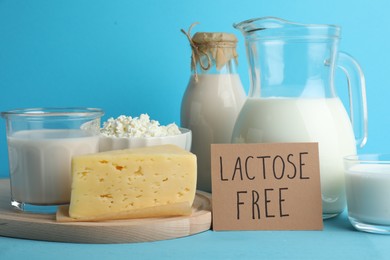 Photo of Dairy products and card with phrase Lactose Free on light blue table