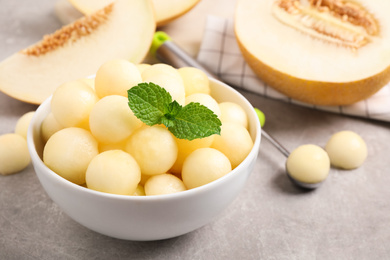 Photo of Melon balls and mint in bowl on light grey table, closeup