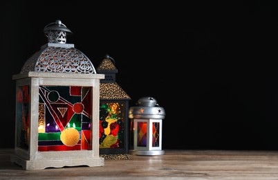 Photo of Decorative Arabic lanterns on wooden table against black background, space for text