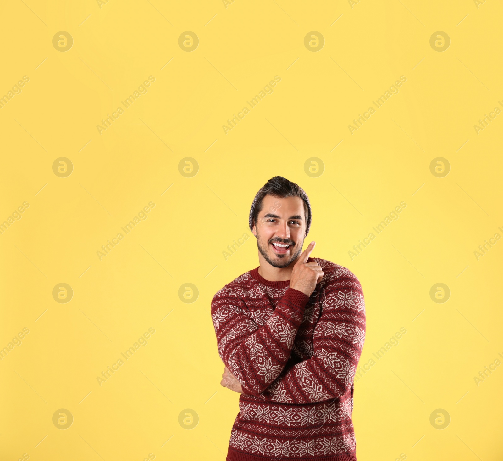 Photo of Portrait of young man in Christmas sweater and hat on yellow background