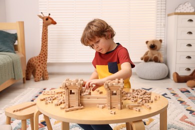 Photo of Little boy playing with wooden entry gate at table in room. Child's toy