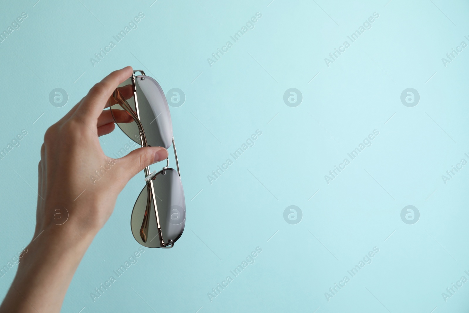 Photo of Woman holding stylish sunglasses on light blue background, closeup. Space for text