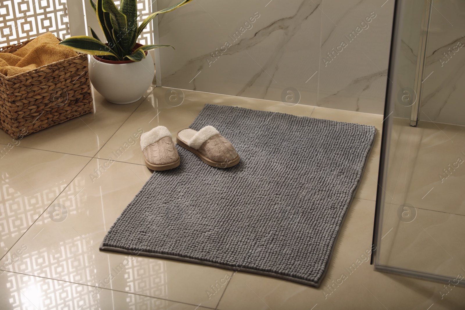 Photo of Soft grey bath mat and slippers on floor in bathroom