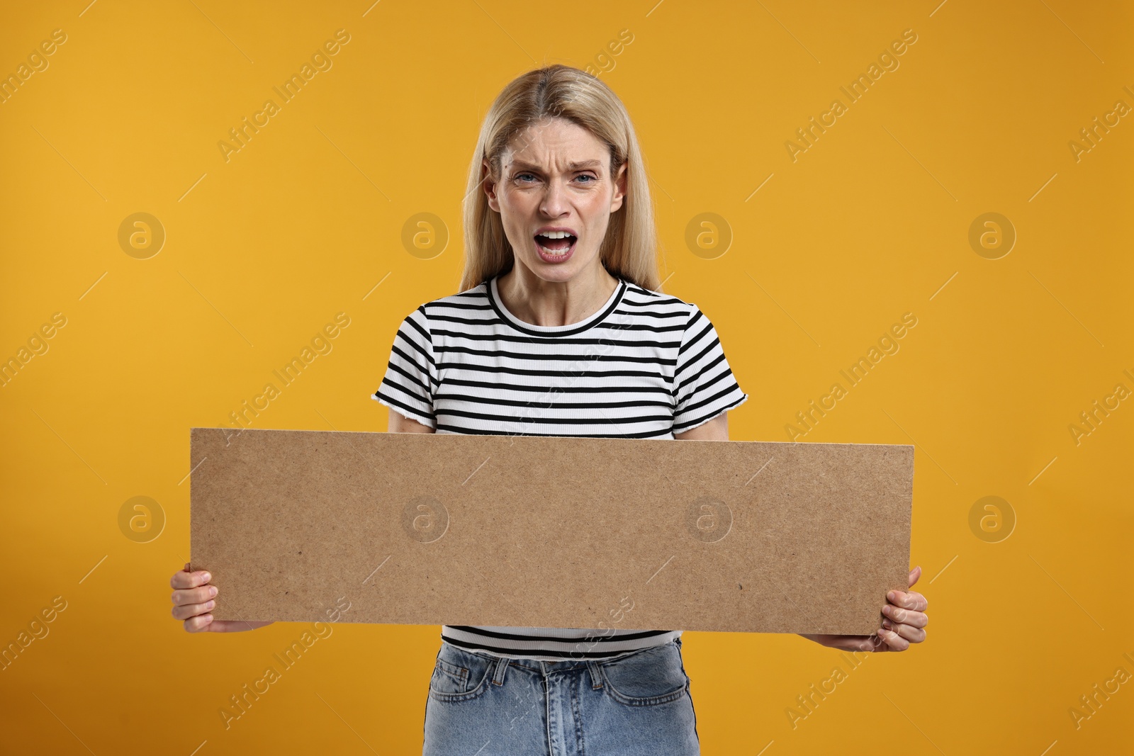 Photo of Angry woman holding blank cardboard banner on orange background, space for text