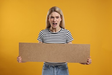Photo of Angry woman holding blank cardboard banner on orange background, space for text