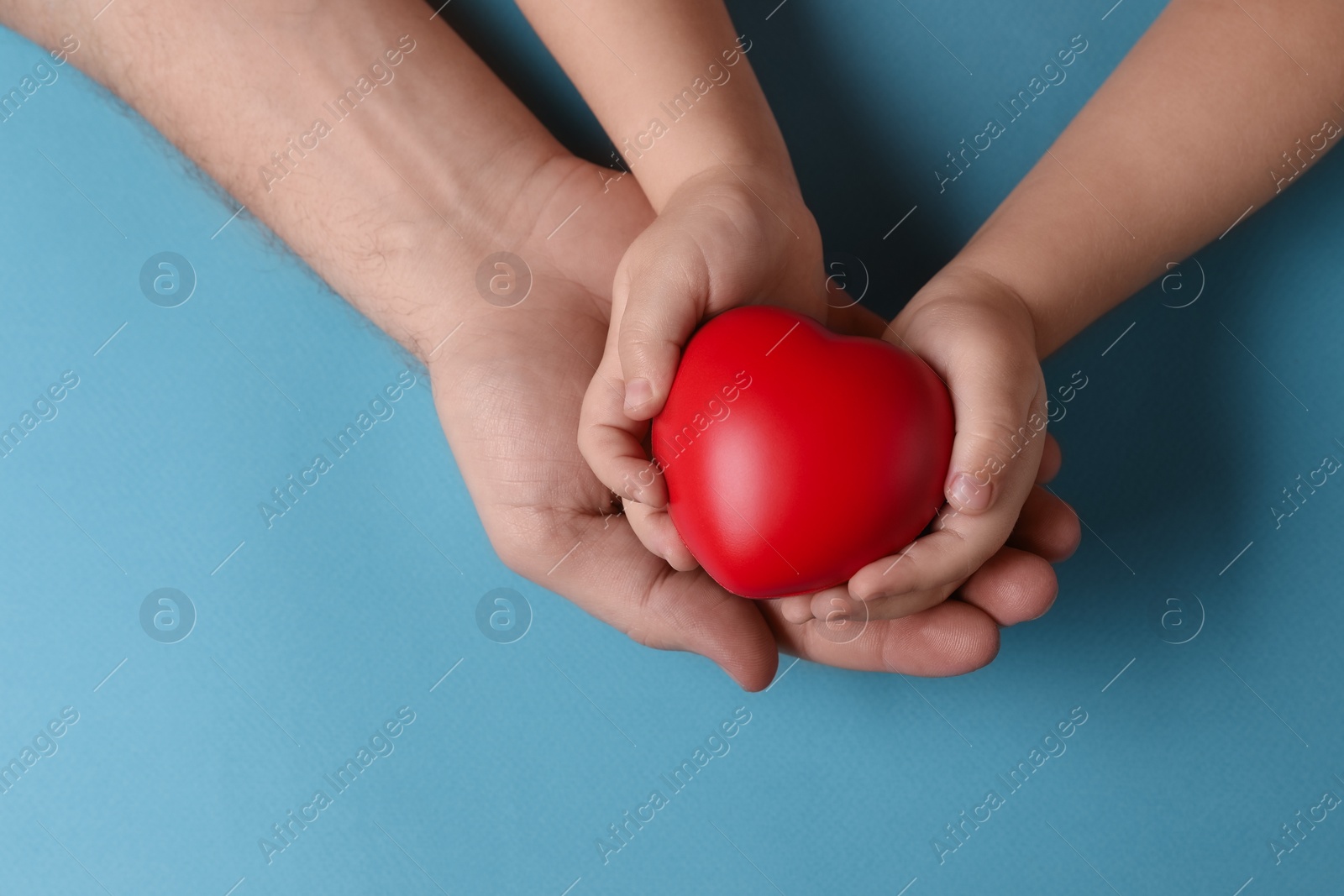 Photo of Father and his child holding red decorative heart on light blue background, top view. Space for text