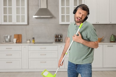 Photo of Happy man in headphones with mop singing while cleaning in kitchen. Space for text