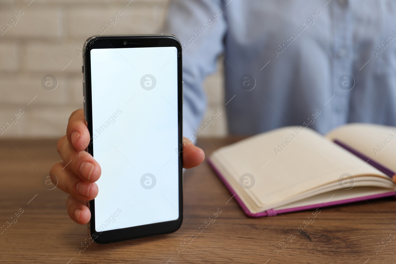 Photo of Woman holding smartphone with blank screen at wooden table, closeup. Space for text