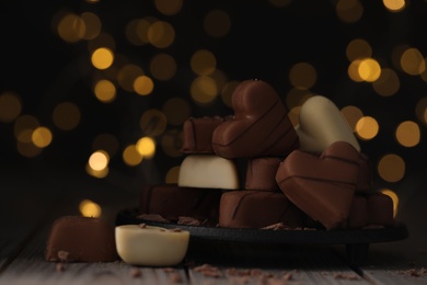Photo of Delicious heart shaped chocolate candies on wooden table against blurred lights