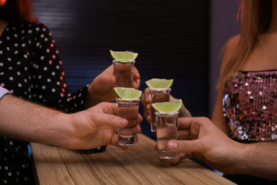 Photo of Young people toasting with Mexican Tequila shots at bar, closeup