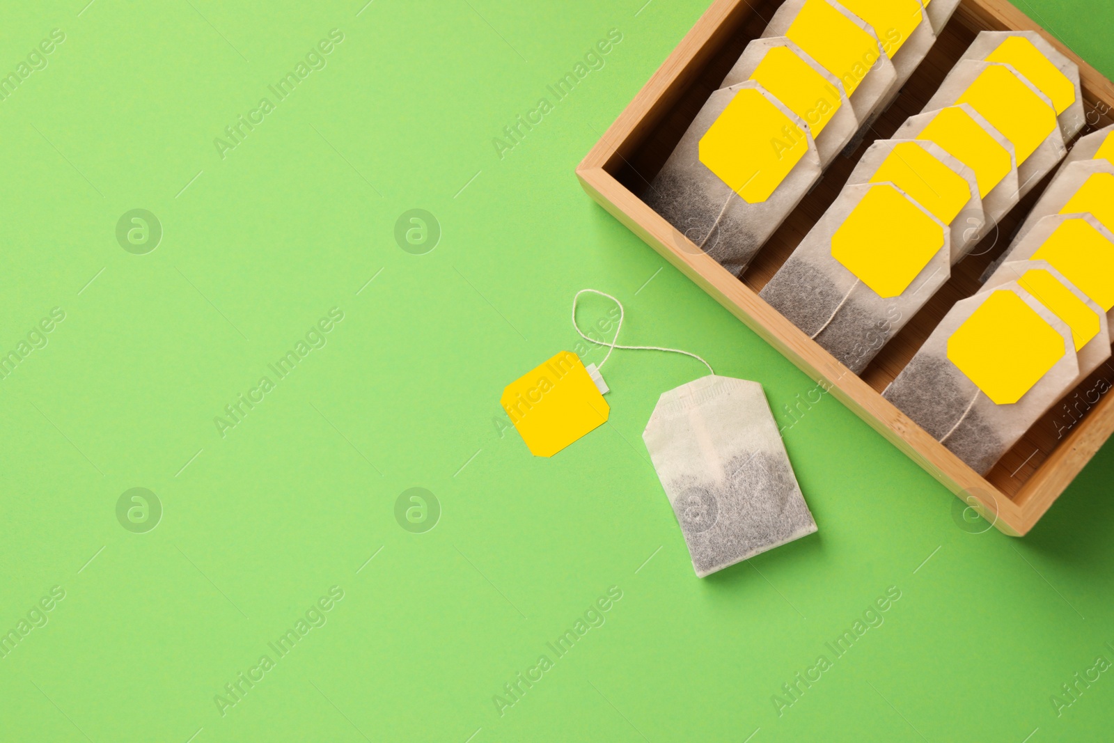 Photo of Many tea bags in wooden box on light green background, flat lay. Space for text