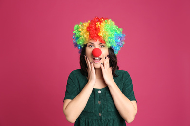 Photo of Emotional woman with rainbow wig and clown nose on pink background. April fool's day