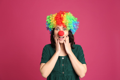 Emotional woman with rainbow wig and clown nose on pink background. April fool's day