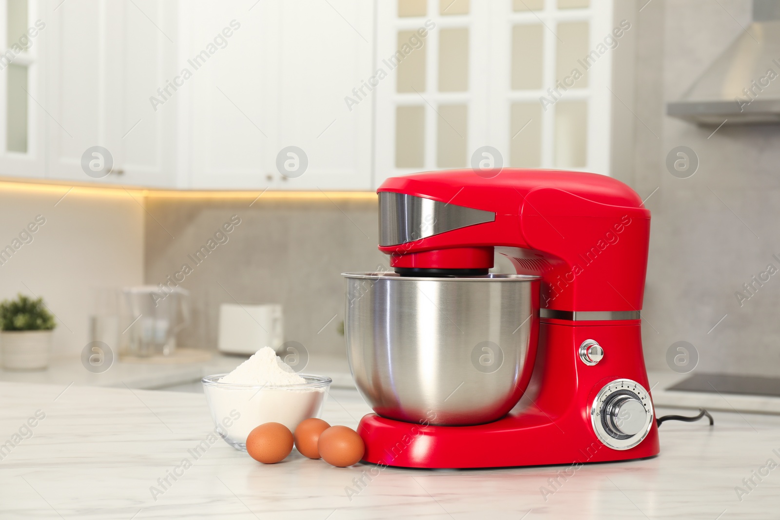 Photo of Modern red stand mixer, eggs and bowl with flour on white marble table in kitchen