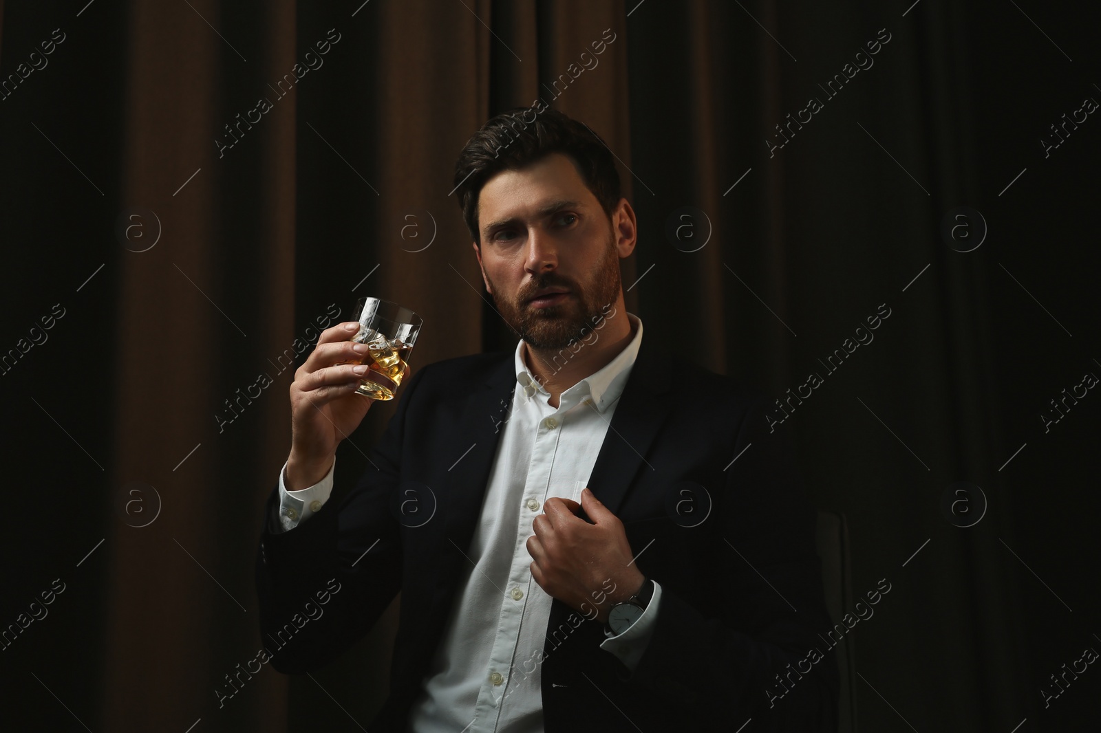 Photo of Man in suit holding glass of whiskey with ice cubes on brown background