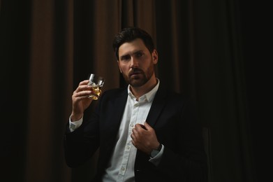 Photo of Man in suit holding glass of whiskey with ice cubes on brown background