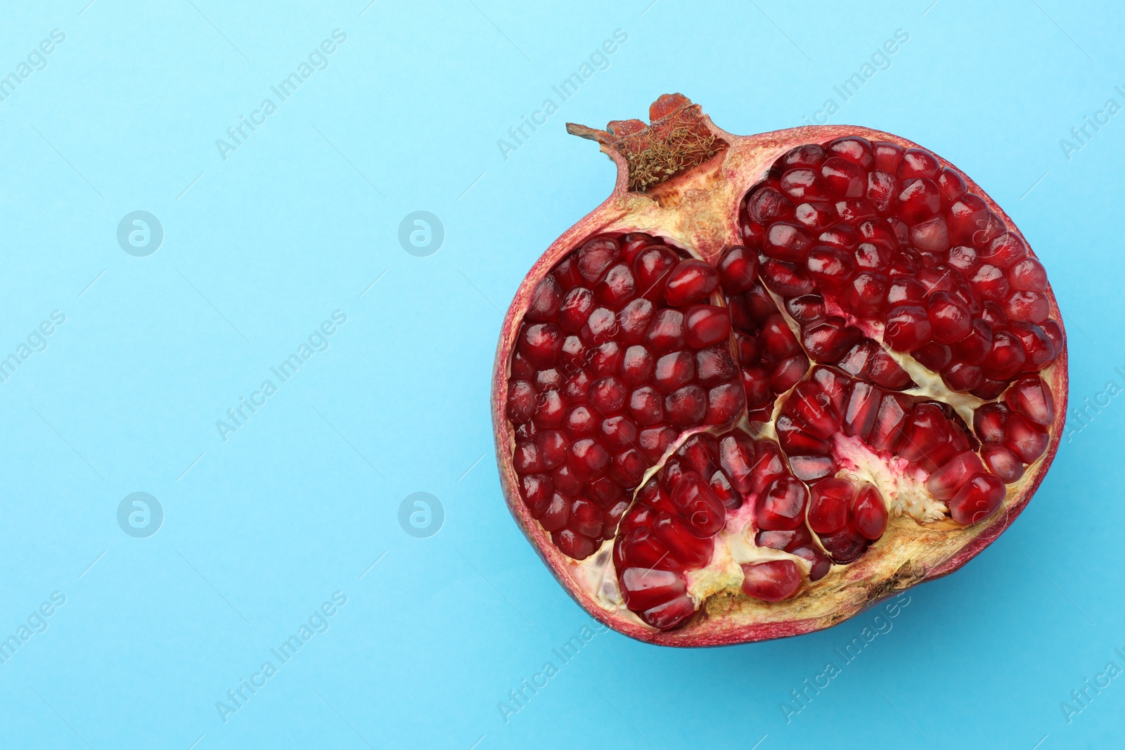 Photo of Cut fresh pomegranate on light blue background, top view. Space for text