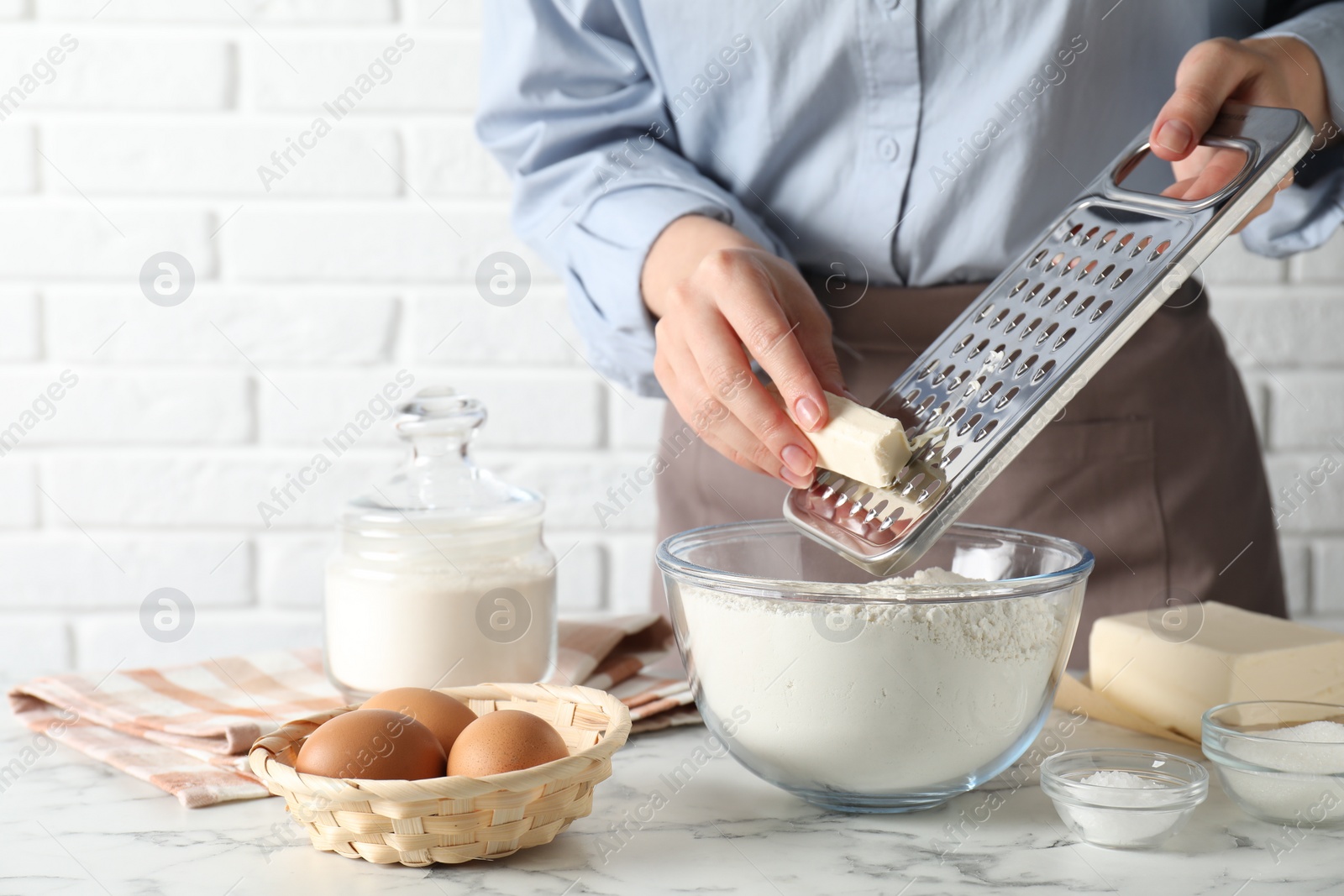 Photo of Woman grating butter into bowl with flour at white marble table, closeup