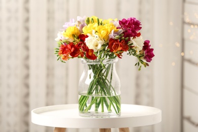 Photo of Vase with beautiful bright freesia flowers on table in room