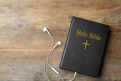 Photo of Bible and earphones on wooden background, top view. Religious audiobook