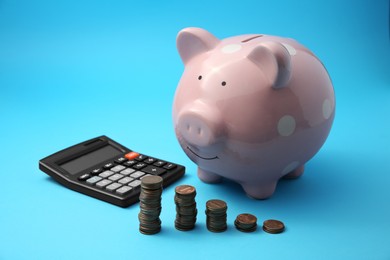 Photo of Piggy bank, stacks of coins and calculator on light blue background