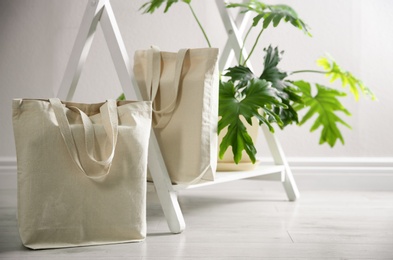 Photo of Eco bags and houseplant near white wall indoors. Space for design