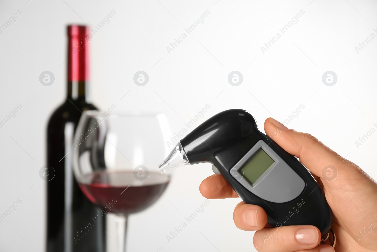 Photo of Woman holding modern breathalyzer with blank screen near wine on light background, closeup