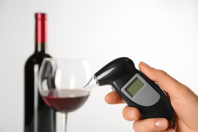 Woman holding modern breathalyzer with blank screen near wine on light background, closeup