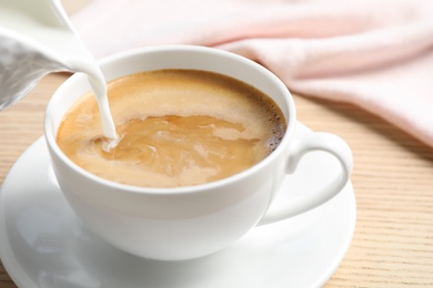 Photo of Pouring milk into cup of hot coffee on wooden table, closeup