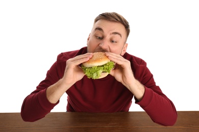 Young man eating tasty burger at table on white background