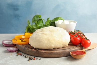 Fresh dough and ingredients for pizza on table against color background