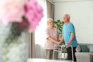 Photo of Elderly woman and her husband with walking frame indoors