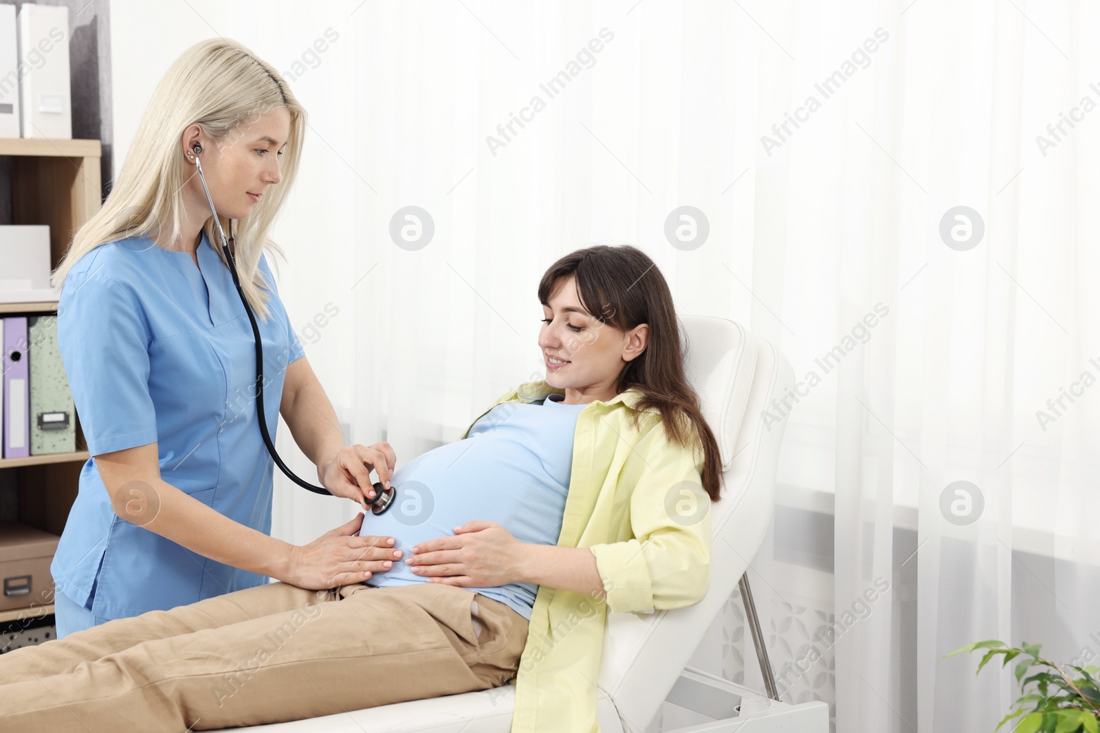 Photo of Pregnancy checkup. Doctor with stethoscope listening baby's heartbeat in patient's tummy in clinic