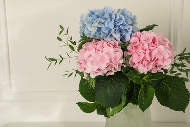 Photo of Beautiful hortensia flowers in vase near white wall. Space for text