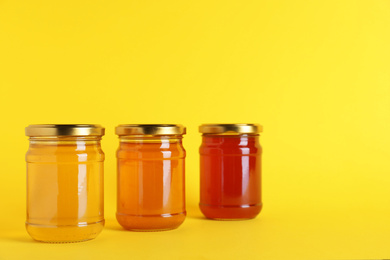 Photo of Jars with different types of organic honey on yellow background
