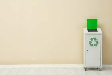 Trash bin with recycling symbol near color wall indoors. Space for text