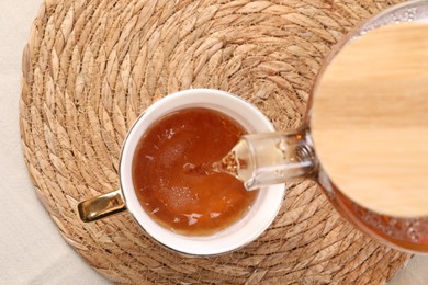 Photo of Pouring aromatic tea into cup at table, top view
