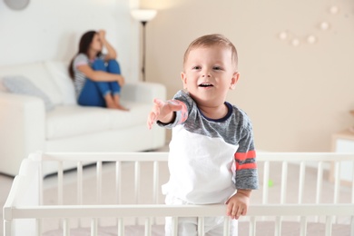 Photo of Cute baby boy in crib and young mother suffering from postnatal depression on blurred background