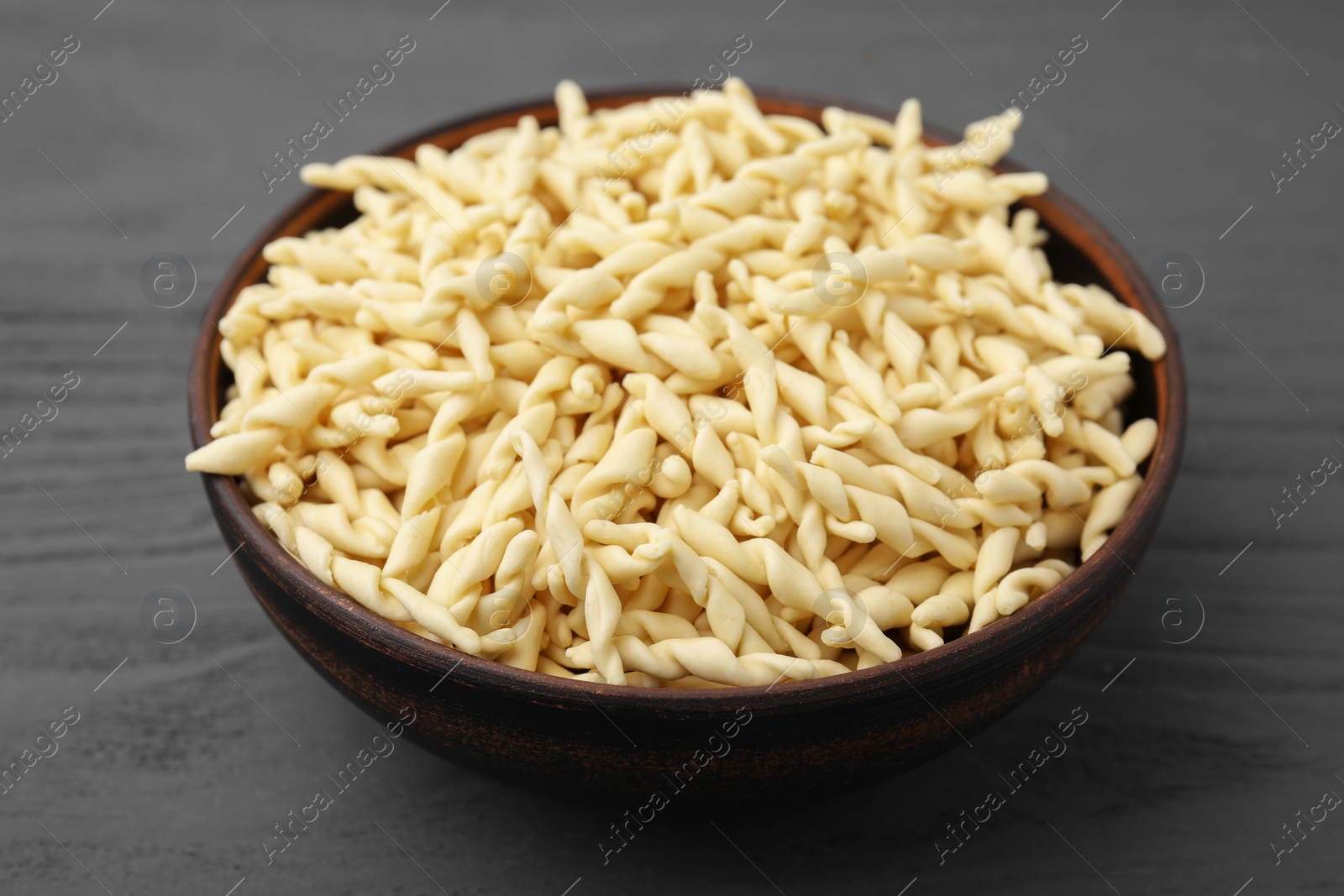 Photo of Uncooked trofie pasta in bowl on grey wooden table, closeup