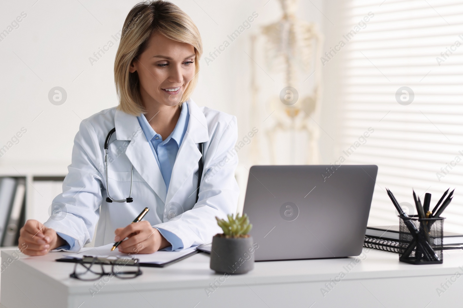 Photo of Smiling doctor with laptop having online consultation at table in office