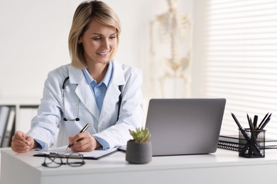 Smiling doctor with laptop having online consultation at table in office