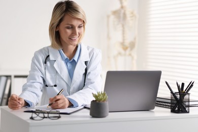 Photo of Smiling doctor with laptop having online consultation at table in office