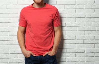 Young man wearing blank t-shirt near white brick wall, closeup. Mockup for design