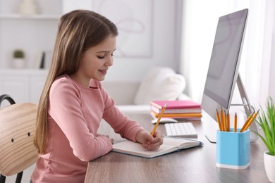 Photo of E-learning. Cute girl taking notes during online lesson at table indoors