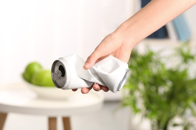 Photo of Woman holding crumpled aluminum can on blurred background. Metal waste recycling