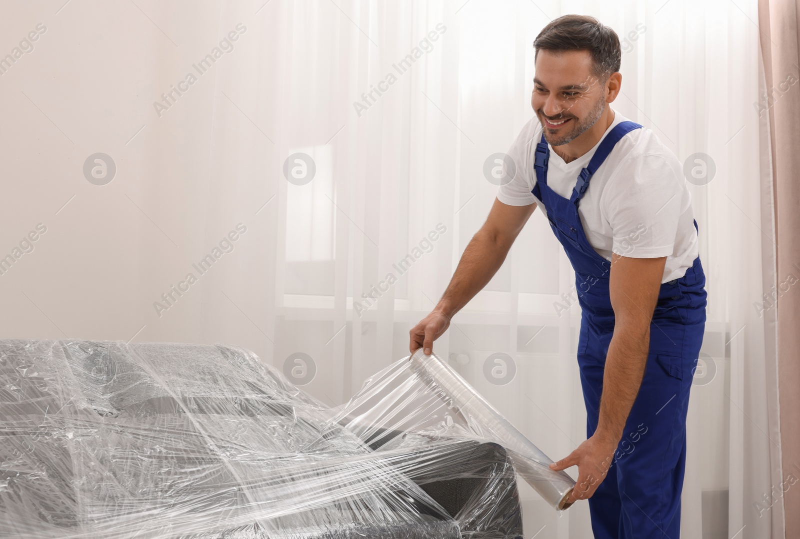 Photo of Worker wrapping sofa in stretch film indoors