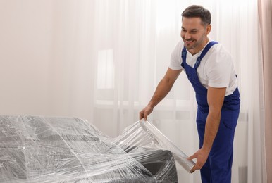 Worker wrapping sofa in stretch film indoors